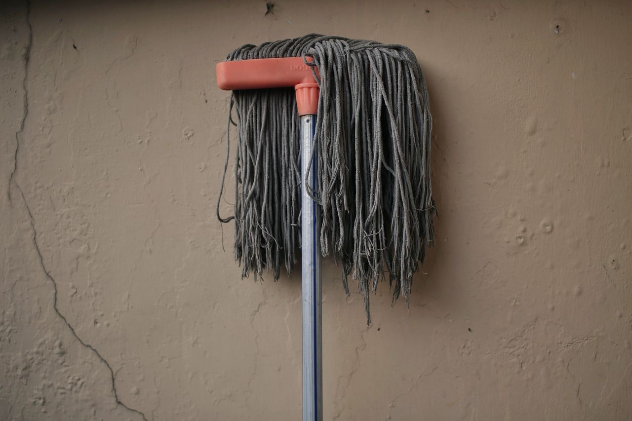 gallery-03 A gray mop is propped against a textured wall, suggesting a simple scene in a home setting.